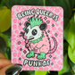 A pink possum character with it's tongue out, a green mohawk and wearing a green spikey necklace against a pink cheetah print background with the words "Being Queer is Punk AF"