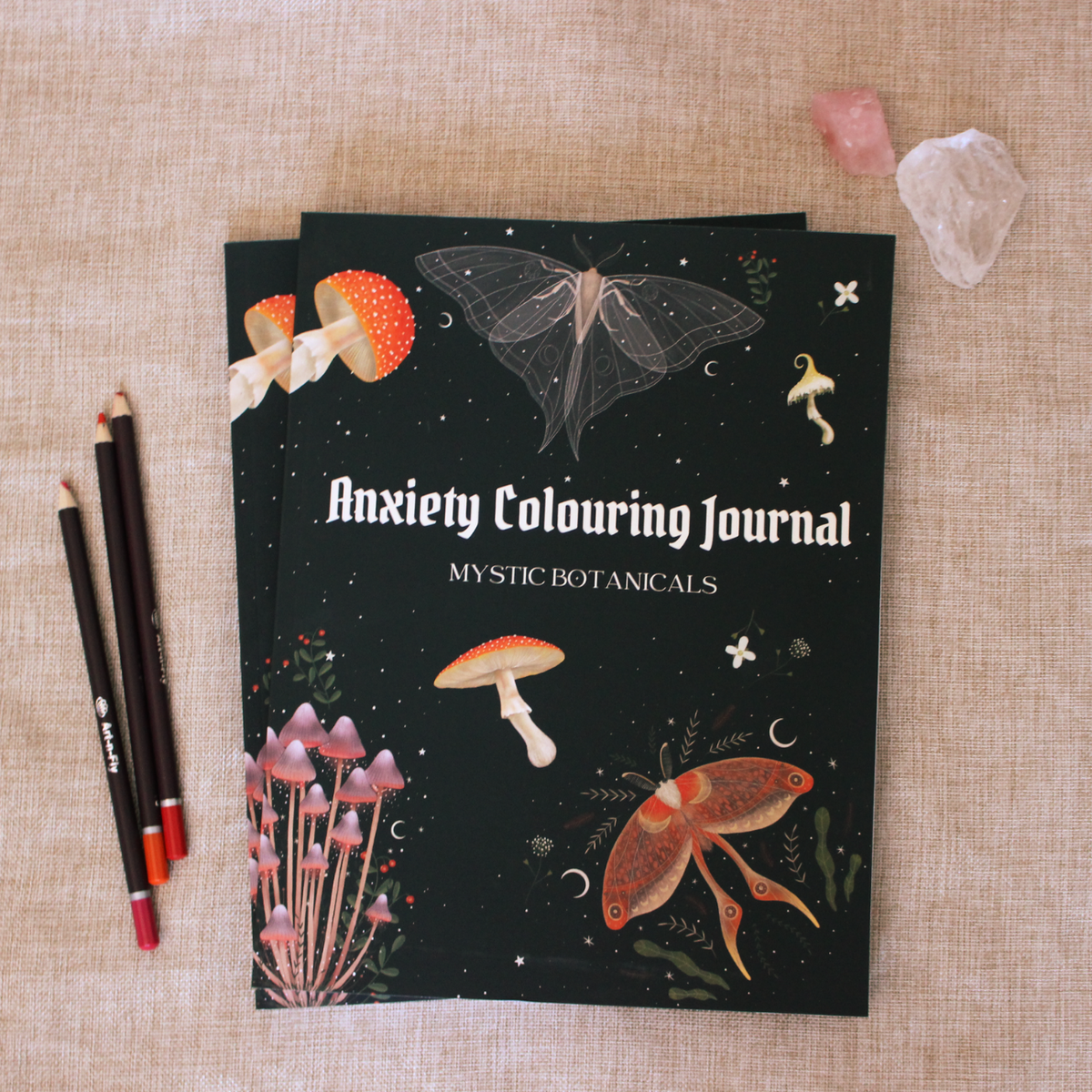 Anxiety Colouring Journal titled 'Mystic Botanicals' placed on a surface with coloring pencils and decorative crystals.