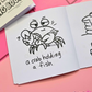 Mini colouring book page featuring a crab holding a fish with the caption "a crab holding a fish."