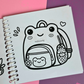 Mini frog-themed colouring book page featuring a cute frog-shaped backpack with a matching frog pouch, flower charm, and mushroom drink bottle.