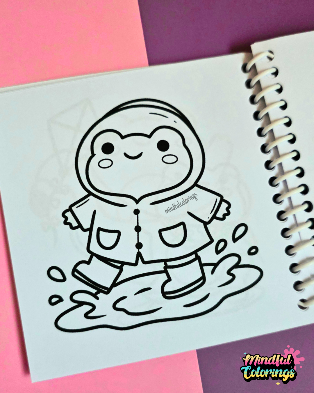 Mini frog-themed colouring book page featuring a cheerful frog wearing a raincoat and rain boots while splashing in a puddle.