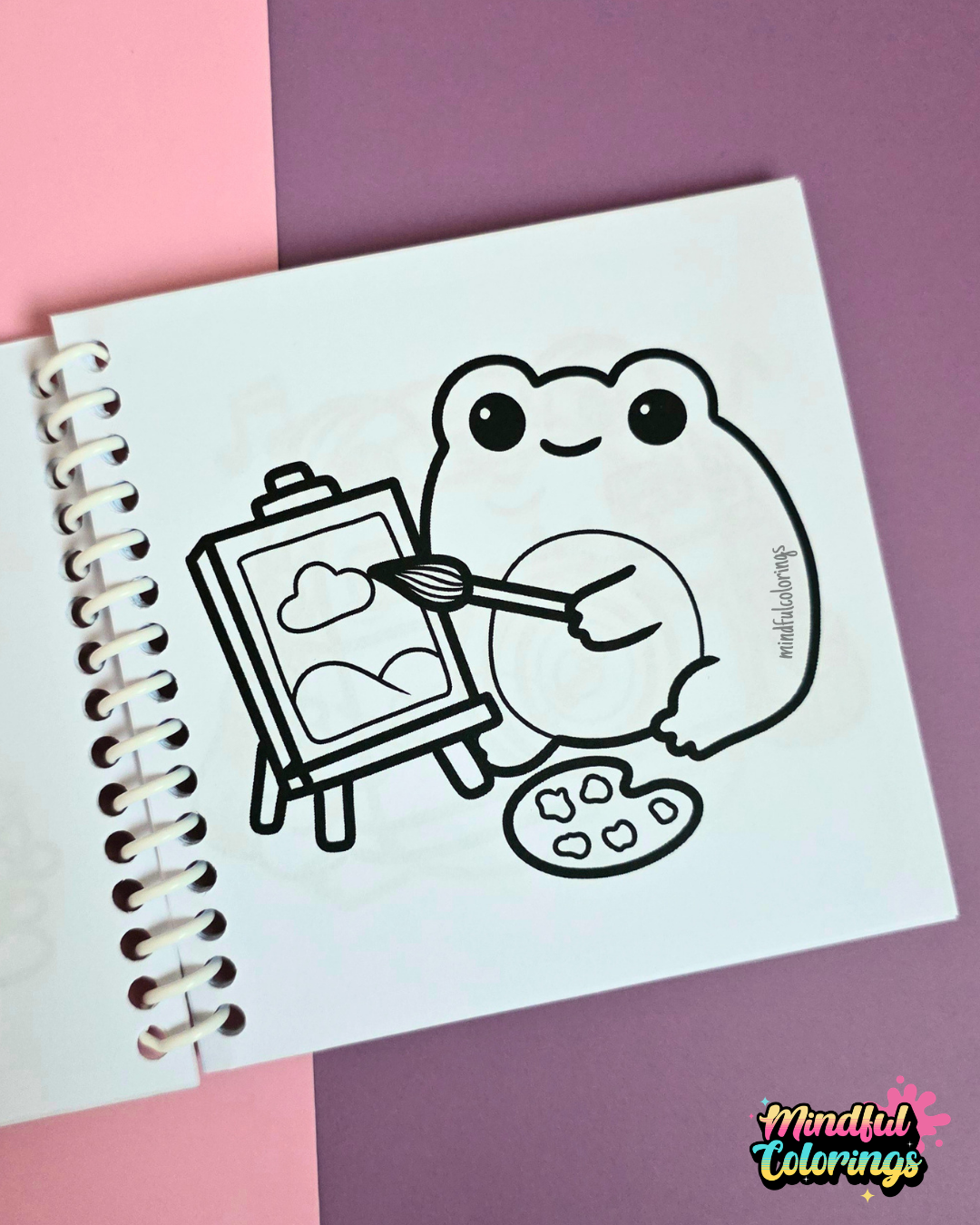 Mini frog-themed colouring book page featuring a creative frog painting a picture on an easel while holding a paintbrush and artist palette.