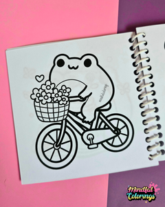 Mini frog-themed colouring book page featuring a happy frog riding a bicycle with a basket full of flowers.