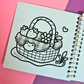 Mini frog-themed colouring book page featuring a picnic basket decorated with a frog face, filled with strawberries, flowers, and cozy frogcore details.