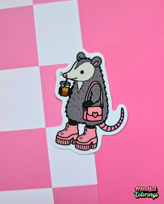 Cute opossum vinyl sticker holding an iced coffee and wearing pink platform boots with a matching heart purse on a pink background.