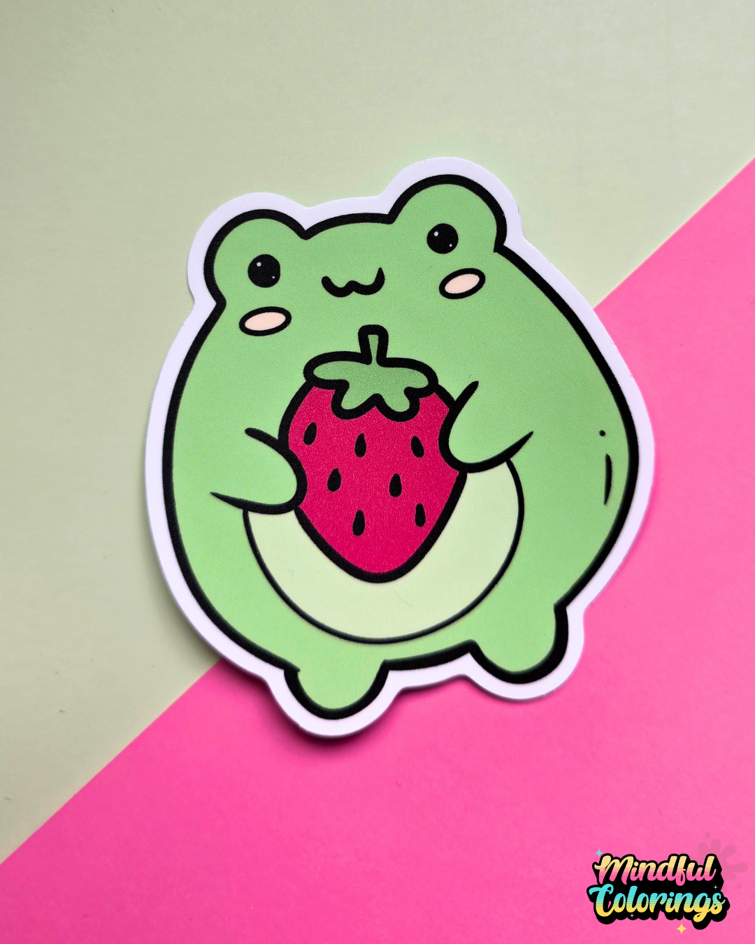 Waterproof vinyl sticker featuring a cute green frog holding a large strawberry on a pink and mint background.