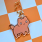 Close-up of a chubby orange cat looking concerned. Acrylic keychain with a gold cat-shaped clasp on an orange checkered background.