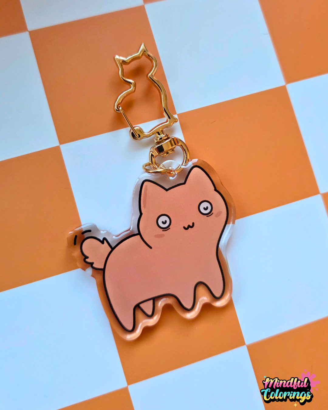 Close-up of a chubby orange cat looking concerned. Acrylic keychain with a gold cat-shaped clasp on an orange checkered background.