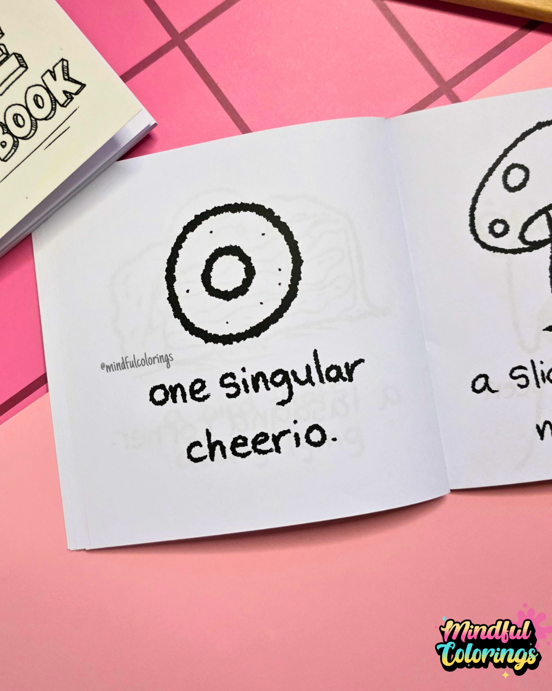Mini coloring book with a black and white illustration of a cheerio that says "a single cheerio" on a pink surface