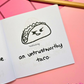 Mini coloring book with a taco and text  that says "an untrustworthy taco" on a pink surface