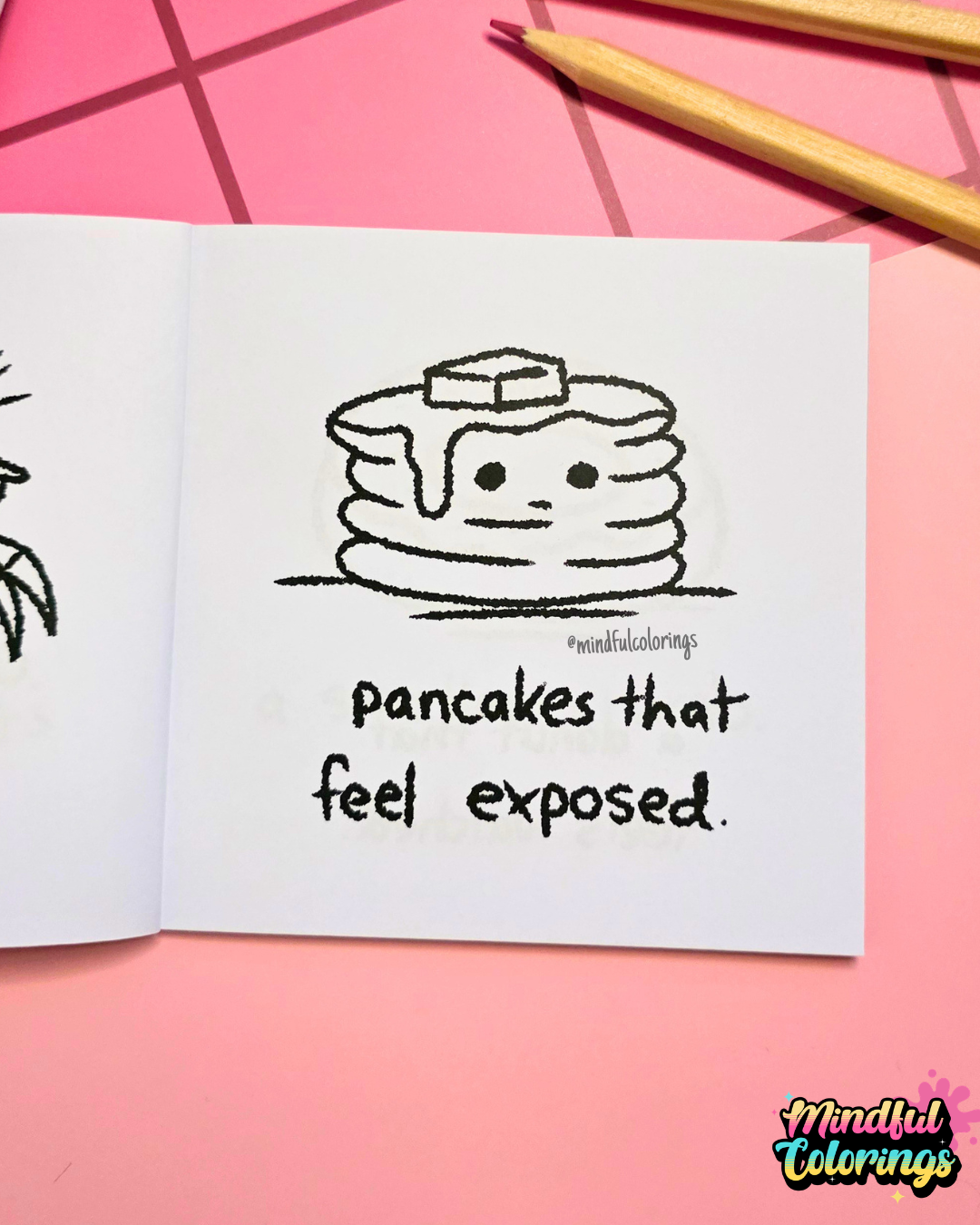 Mini coloring book with a drawing of pancakes and text 'pancakes that feel exposed' on a pink surface