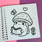 Mini frog-themed colouring book page featuring a cute frog reading a book while sitting beneath a spotted mushroom, surrounded by a butterfly, flower, and heart.