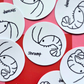 Flat lay of multiple round Shramp vinyl stickers featuring a simple hand-drawn shrimp illustration on a pink background.