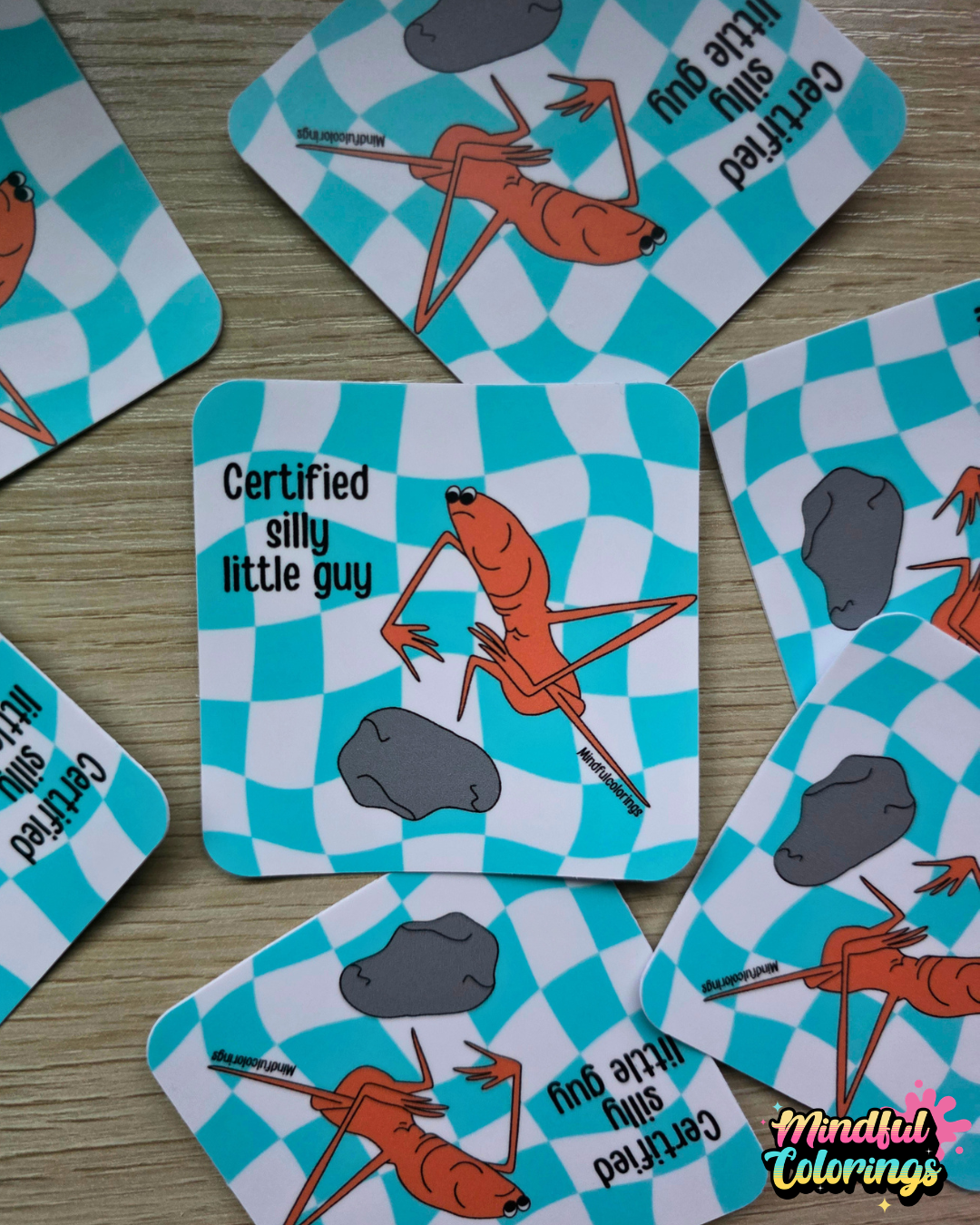 Stickers with the viral Marcus the Worm character crouched next to a rock with the text "Certified Silly Little Guy" with a blue checkered background