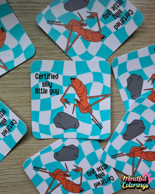 Stickers with the viral Marcus the Worm character crouched next to a rock with the text "Certified Silly Little Guy" with a blue checkered background