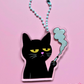 Black cat acrylic keychain featuring a grumpy cat holding a cigarette with smoke rising above it, attached to a white beaded clasp on a pink background.