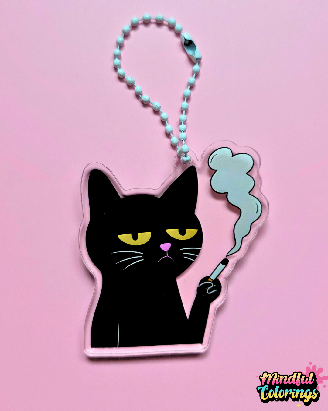 Black cat acrylic keychain featuring a grumpy cat holding a cigarette with smoke rising above it, attached to a white beaded clasp on a pink background.