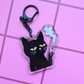 Acrylic keychain featuring a grumpy black cat holding a cigarette with smoke rising above it on a pink 
