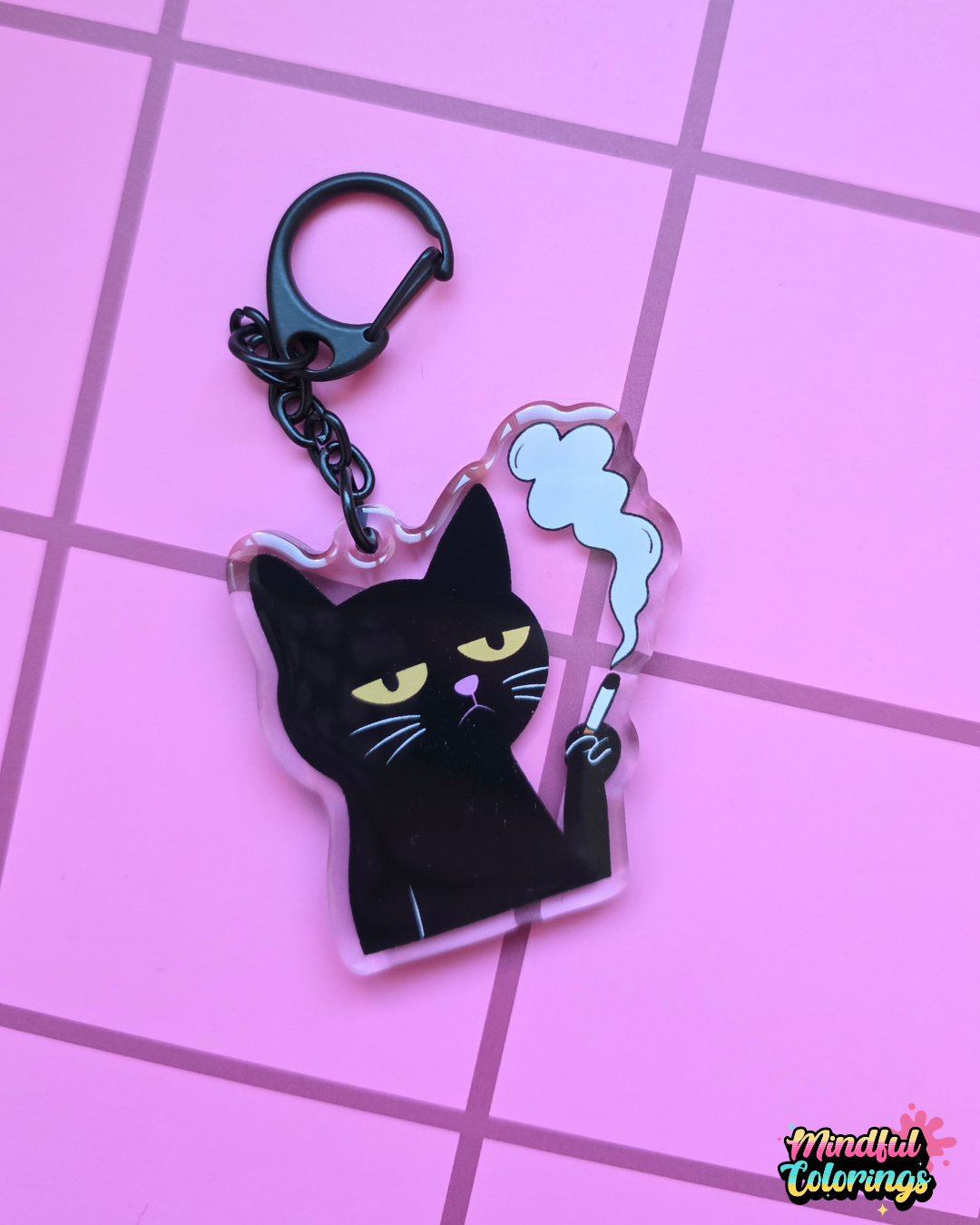 Acrylic keychain featuring a grumpy black cat holding a cigarette with smoke rising above it on a pink 