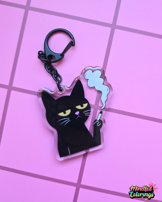 Acrylic keychain featuring a grumpy black cat holding a cigarette with smoke rising above it on a pink 