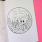 An open coloring book showing a black-and-white circular campsite scene with a masked figure, trees, mountains, and a campfire. The page is placed on a bright pink background, with a small 'Mental Colorings' logo in the bottom right corner.