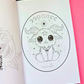An open coloring book or art booklet showing a black-and-white line drawing of a cute baphomet inside an oval frame, placed on a bright pink background with part of another page visible on the left.
