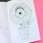 An open coloring book showing a black-and-white line art illustration of a flower with a large eye in the center, placed on a pink and black background. A 'Mindful Colorings' logo is visible in the bottom right corner.