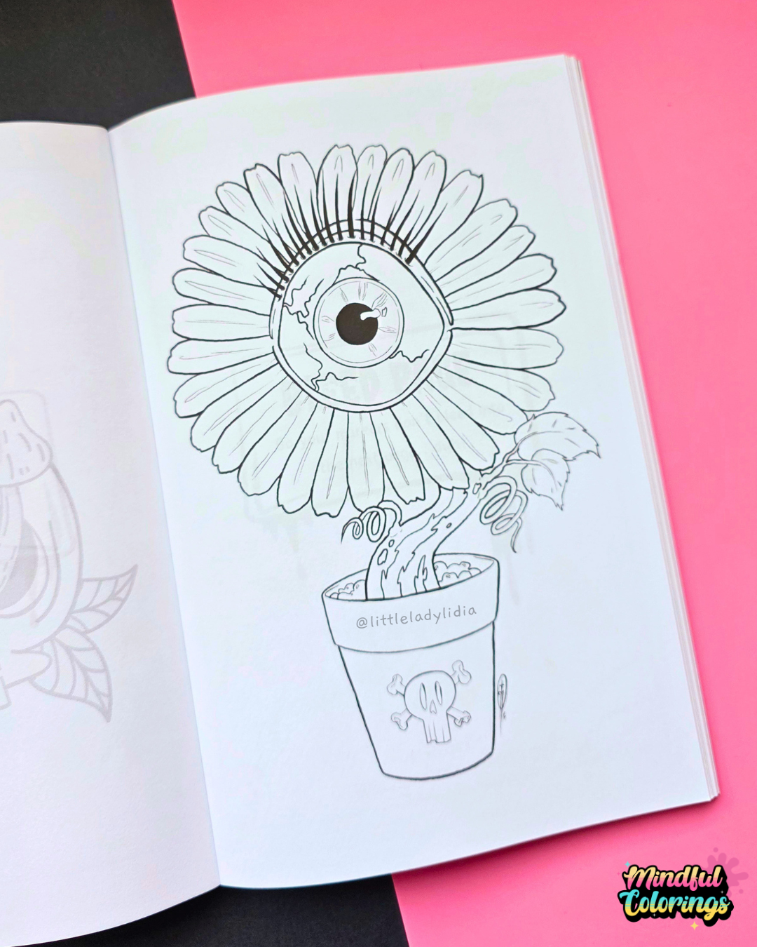 An open coloring book showing a black-and-white line art illustration of a flower with a large eye in the center, placed on a pink and black background. A 'Mindful Colorings' logo is visible in the bottom right corner.