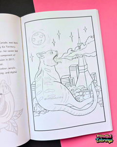 An open coloring book or art journal showing a black-and-white line drawing of a cat-shaped cityscape with stars and a moon, placed on a pink background with a black section visible on the left.