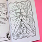 An open coloring book showing a black and white line art illustration of a girl sitting inside a tent under a tree with Blair Witch Movie totems. The book is placed on a bright pink background with a black section visible on the left.