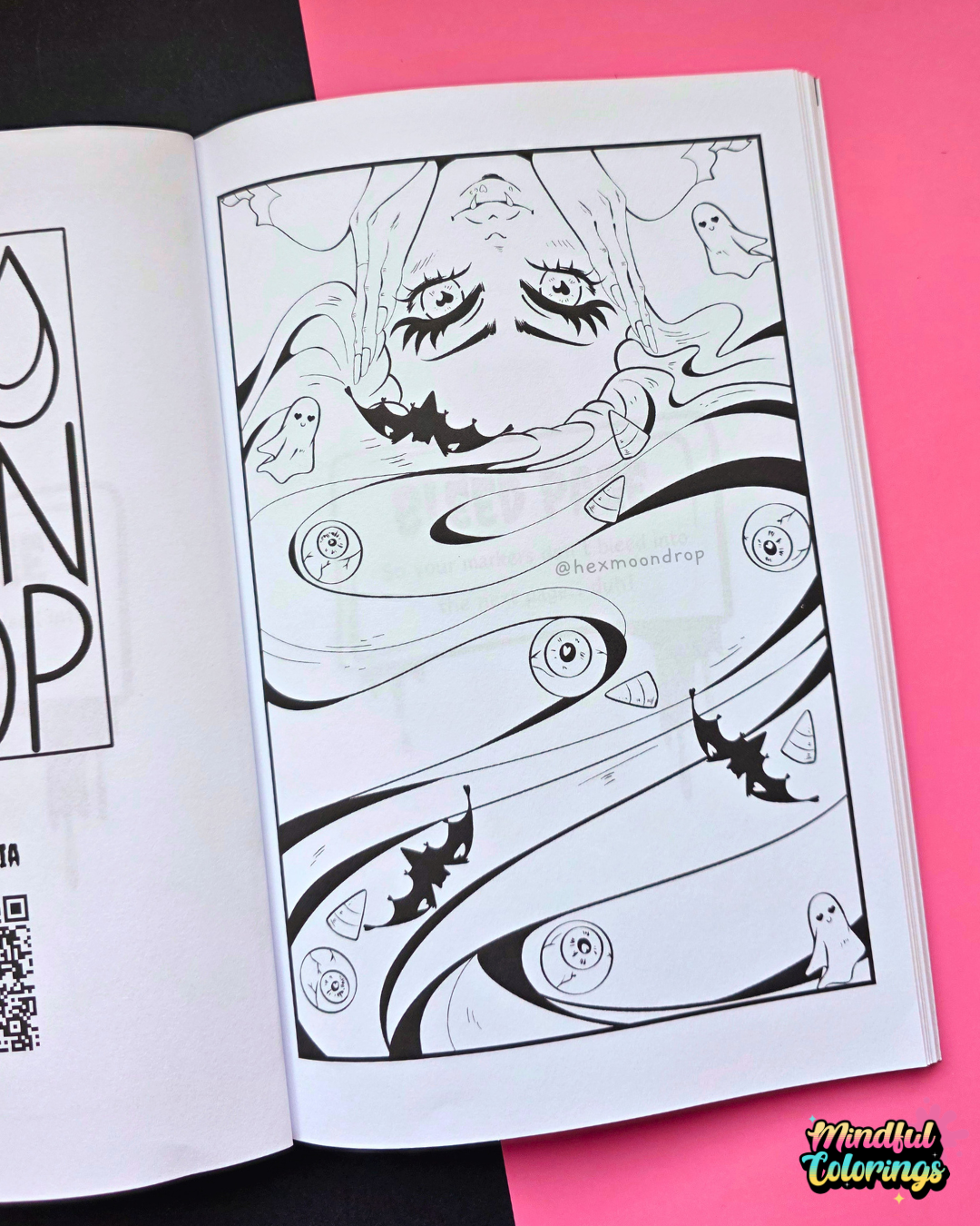 An open coloring book or art booklet showing a black-and-white illustrated page with abstract faces, eyes, and small ghost-like figures, placed on a bright pink background with part of another page visible at left.