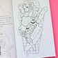 An open coloring book or art booklet showing a black-and-white line drawing of a stylized pregnant woman with cartoon tattoos, placed on a bright pink background with a dark surface visible on the left.