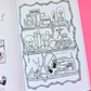 An open coloring book or art booklet showing a black-and-white illustrated page with shelves of occult and gothic objects like a skull, cauldron, books, and mirrors, placed against a bright pink background.