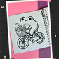 Happy frog riding a bicycle with a basket full of flowers coloring page from the Frogcore Adventures mini coloring book.